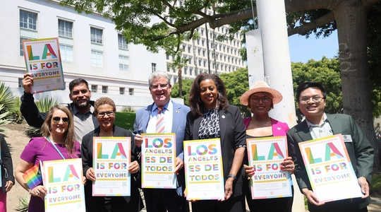 Mayor Karen Bass, Councilmember Imelda Padilla, Councilmember Hugo Soto Martinez, Councilmember Bob Blumenfield, Executive Director Capri Maddox, LGBTQIA+ Community Liaison Carla Ibarra, Commissioner Hoàng Nguyễn standing with LA For All signs during the Progress Pride flag ceremony
