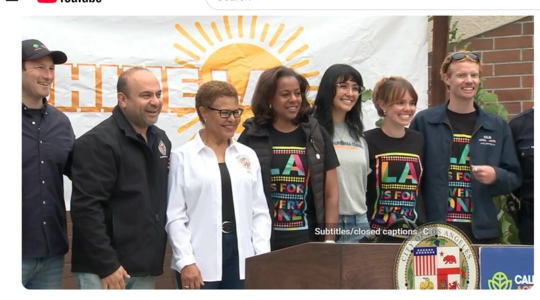 A group including Josh Fryday from the Governor’s Office, LA City Councilmember Adrin Nazarian, LA Mayor Karen Bass, LA Civil Rights Executive Director Capri Maddox, and members of the Tom LaBonge family stand smiling together in front of a Shine LA banner and a City of Los Angeles podium during the Tom LaBonge Day of Service event.