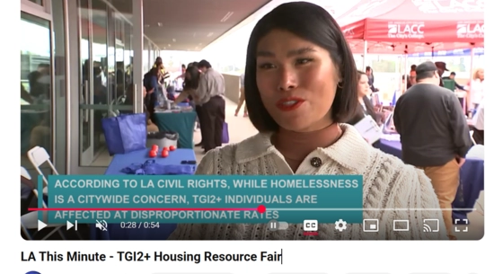 LA Civil Rights LGBTQ+ liaison at TGI2+ Housing Resource Fair speaks about job fair, resource tables and attendees in the background