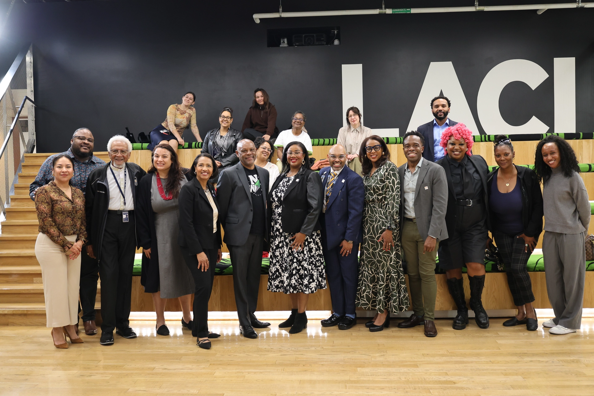 Group photo of panelists and LA Civil Rights staff standing in front of bleachers with guests and LA Clean Incubator LACI logo