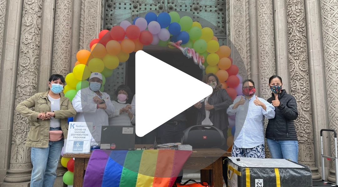 Group photo at the LGBTQ+, Trans & Non-Binary Vaccine Drive with the play button in the foreground, click on it and it takes you directly to youtube to play the video