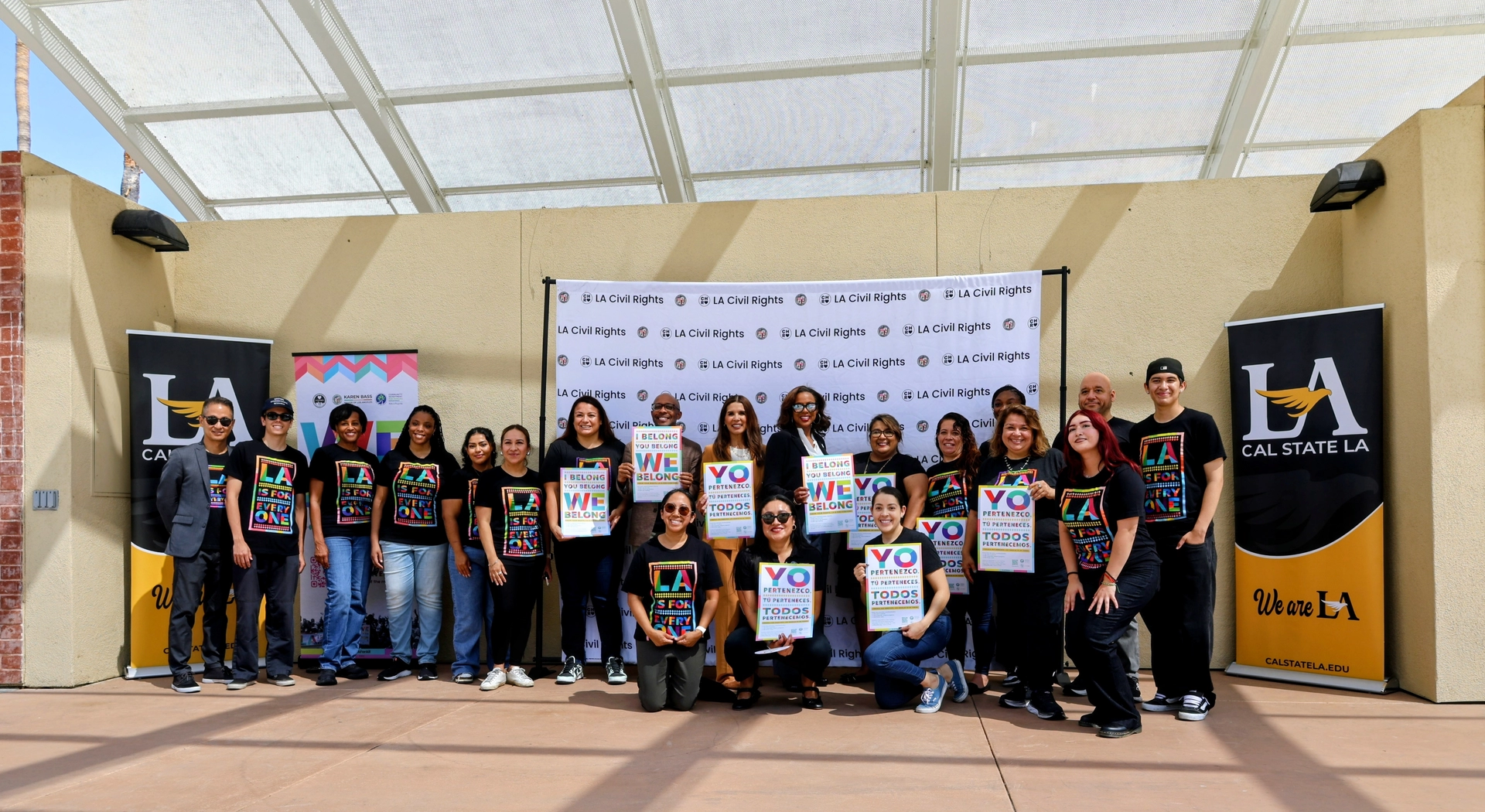 LA Civil Rights staff and volunteers wearing LA is For Everyone t-shirts pose with "We Belong" signs in English and Spanish.