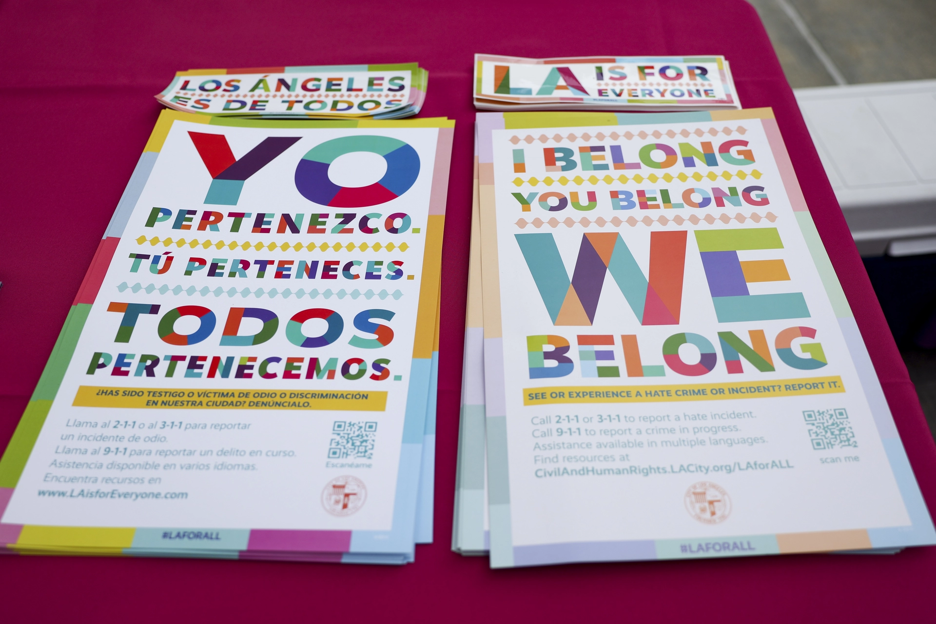 Photograph of posters on a table with I Belong. You Belong. We Belong, in English and in Spanish. 