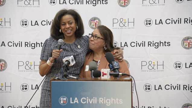 LA Civil Rights Executive Director Capri Maddox stands behind a podium embracing CCNP Executive Director Margarita Alvarez
