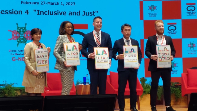 LA Civil Rights Executive Director Capri Maddox stands on stage with four other people holding LA for All posters at the Inclusive & Just Panel at a Conference in Tokyo, Japan.