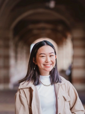Ysabella Sardillo headshot wearing a white top and brown jacket smiling