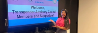 LGBTQIA+ Liaison Carla Ibarra standing in front of monitor that says Welcome to Transgender Advisory Council